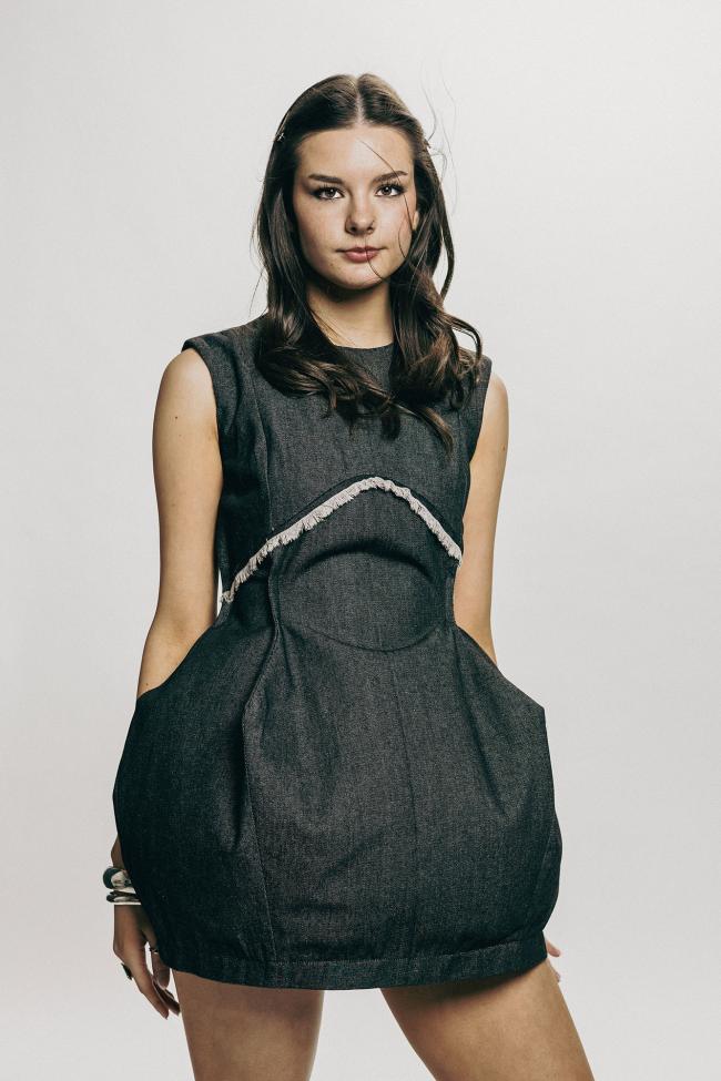 A model wearing a black denim dress with frayed design features.
