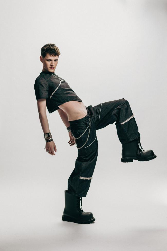 Male model, in an active pose, wearing a black denim top and black denim jeans.