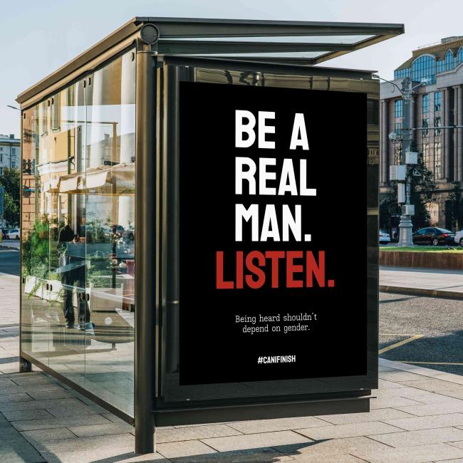 Bus stop advertisement poster with the message “Be a real man. Listen.” displayed in a public urban setting.