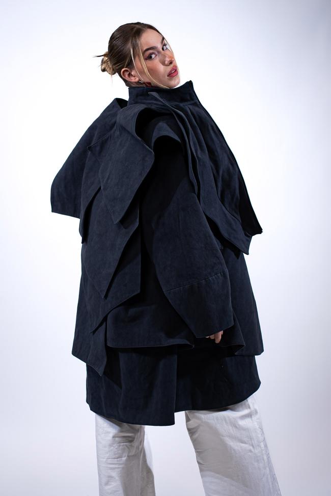 A model wearing a layered draped coat worn with white trousers.