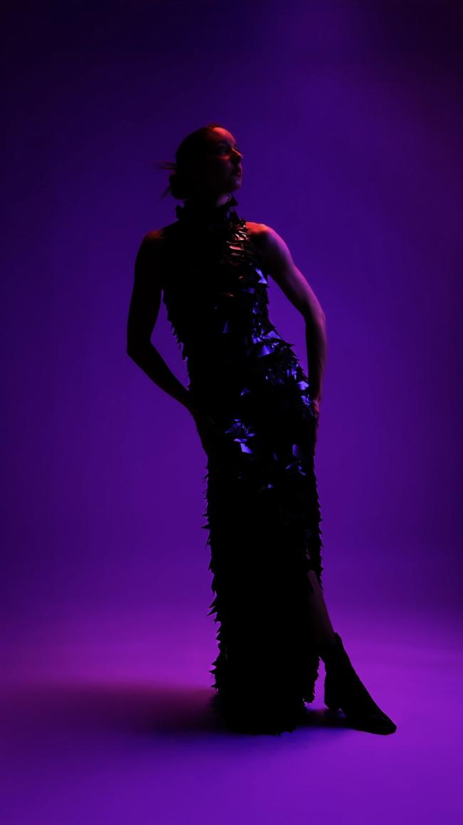 a model wearing a long sparkly dress against a purple background