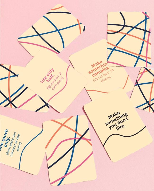 Close-up mockup of the Unprompted prompt cards displayed on a soft pink background. The square cards feature rounded corners and a cream colour palette with abstract flowing line graphics in blue, pink, orange, and black. Several cards are shown face-up with creative prompts designed to encourage experimentation and unconventional thinking. Visible prompts include “Use only half,” “Make something complex,” “Make something you don’t like,” and “One touch only,” each paired with small instructional text expla