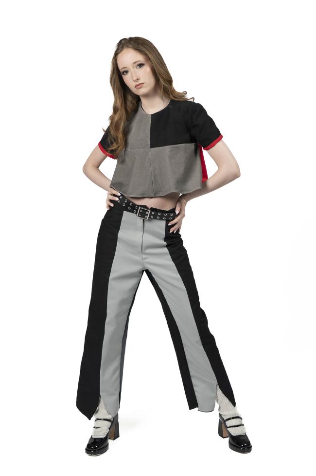 A model in a black, red, and grey top with grey and black panelled trousers.