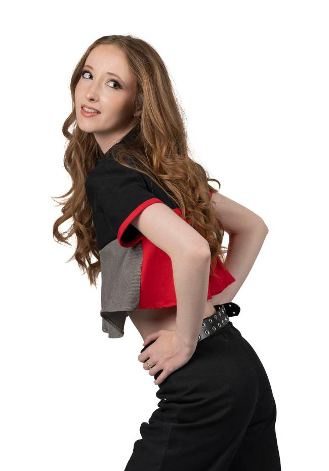 A side view of a female model with long wavy red hair wearing a black, red, and grey top with black trousers