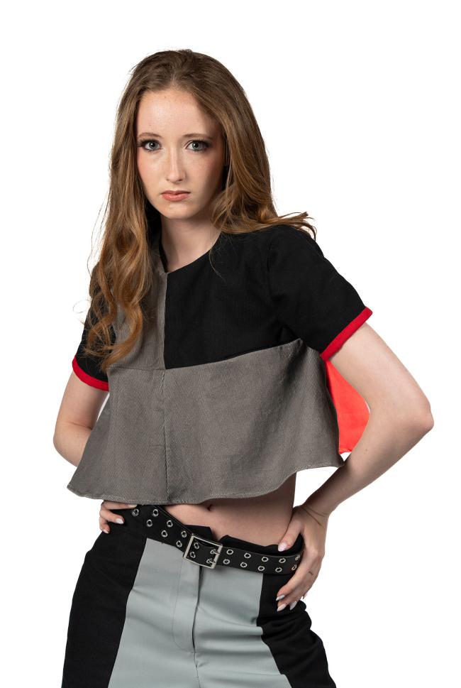  A female model with long wavy red hair wearing a black, red, and grey top with black trousers.