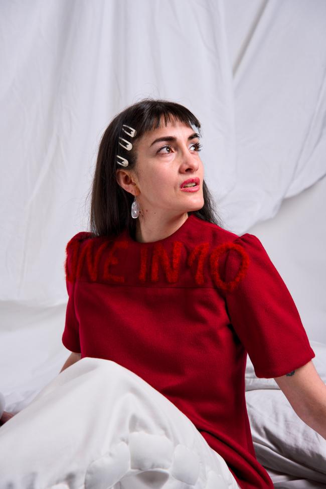 Model in white setting wearing white denim jeans and a red needle felted wool shirt