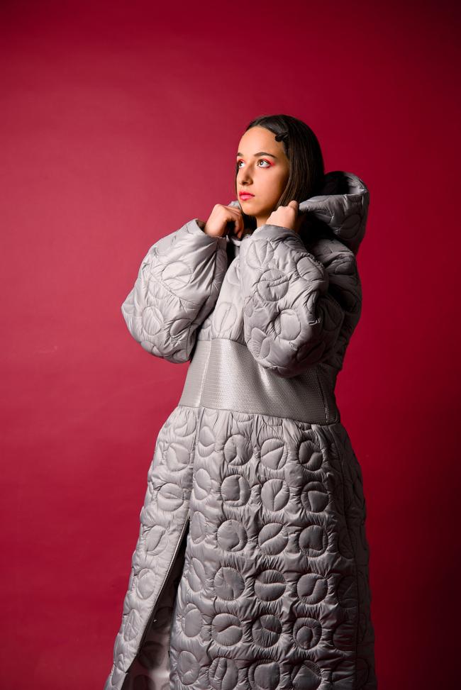 Model in front of a red backdrop wearing a wadded silver coat which hast quilting details