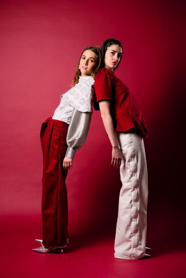 Two models in red and white outfits leaning against each other in a red setting