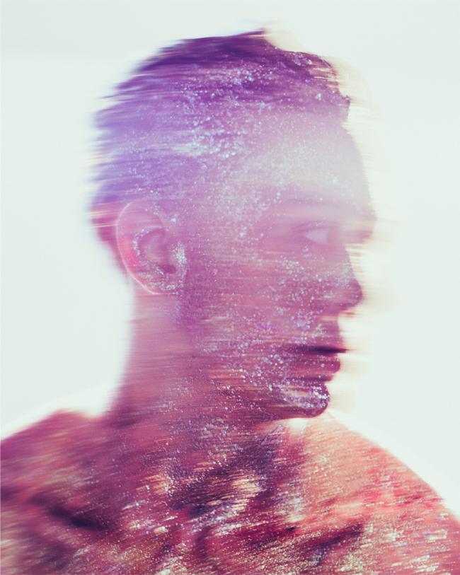 A side-profile portrait of a figure covered in glitter and blurred pink and purple textures creates a dreamlike, abstract effect.