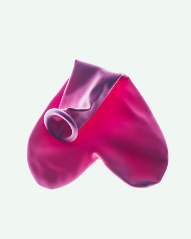 A close-up still life of two pink balloons, one partially deflated, against a pale background.