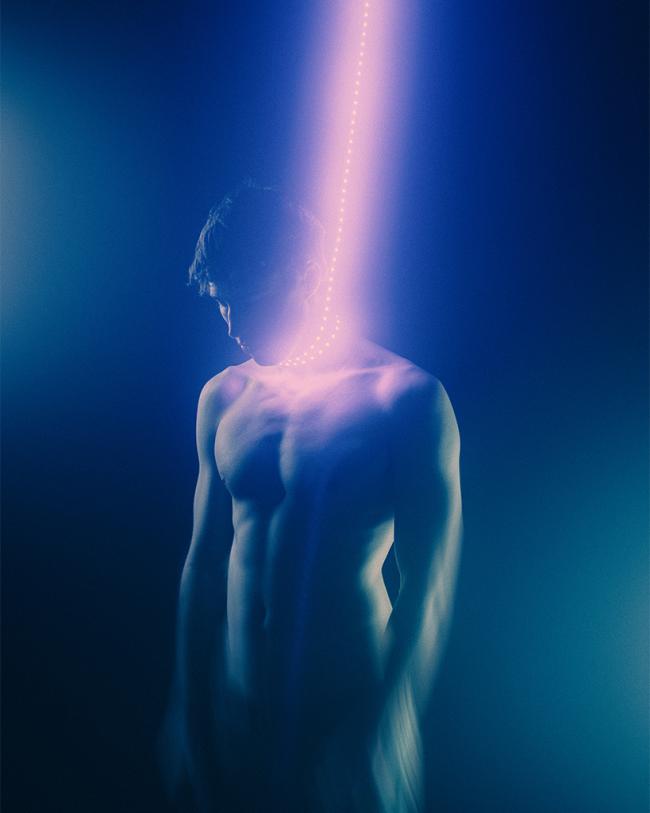 A softly lit portrait of a shirtless figure in blue and purple light with intentional blur and a glowing vertical light element.