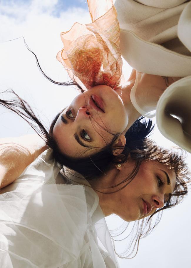 Close-up of two models with sky background and wind blowing their hair and scarf.