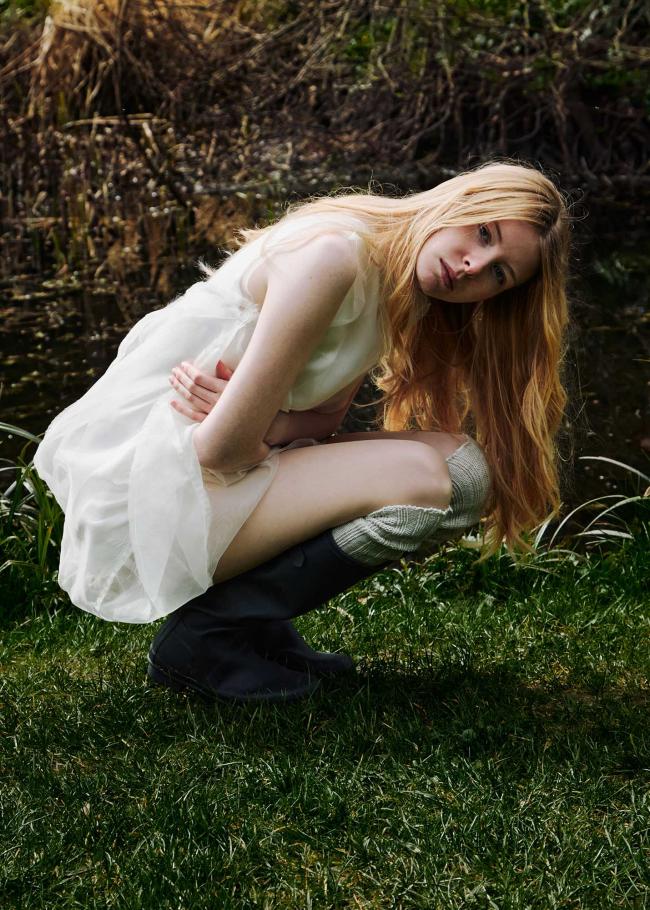 Model crouching in a bubble dress and wellies with a pond in the background.