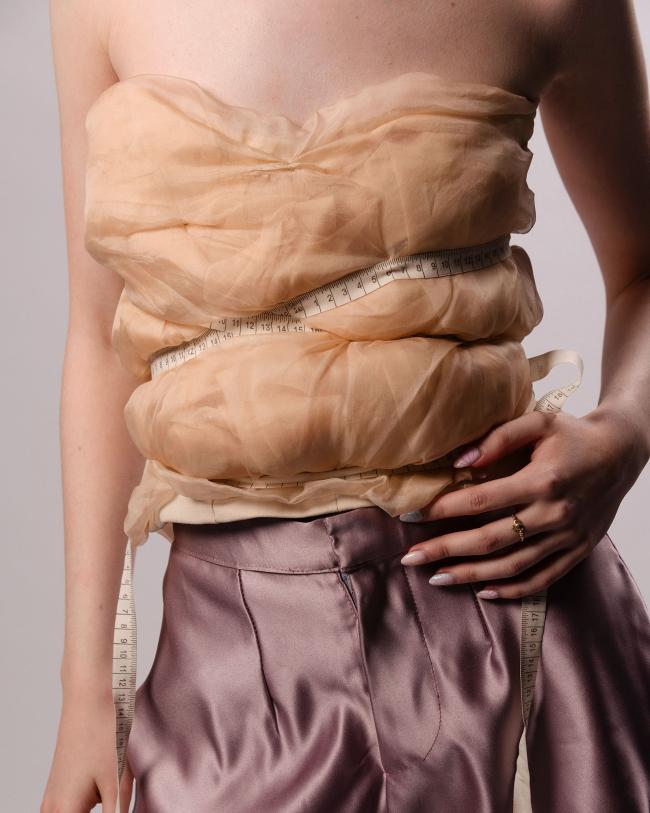 Close-up of beige draped silk corset top with measuring tape ribbon as a feature
