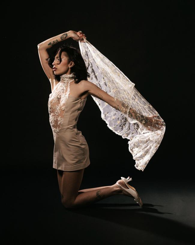 Third model kneeling on the floor wearing a beige lace-detailed minidress and holding a white veil 