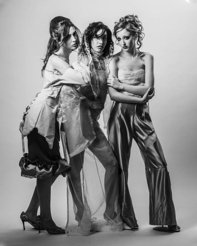 Three models wearing flowing satin and silk outfits with lace detailing, against a white backdrop