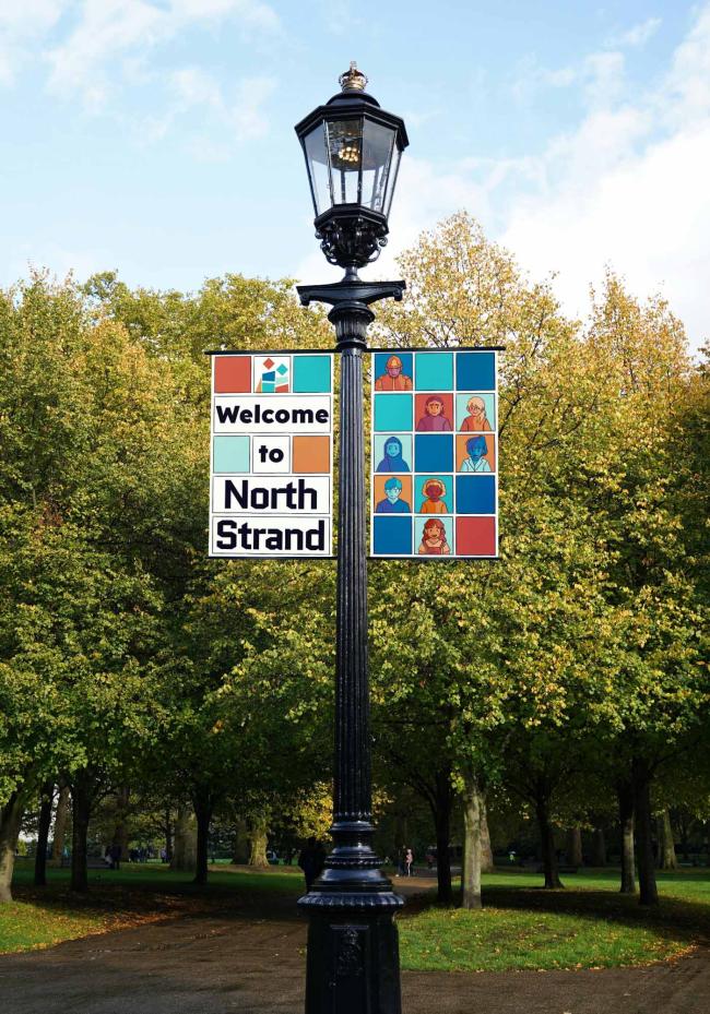 Two street lamp banners with a collage of people in a cartoon style and a caption “Welcome to North Strand”.
