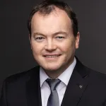 a man wearing a suit and tie smiling at the camera