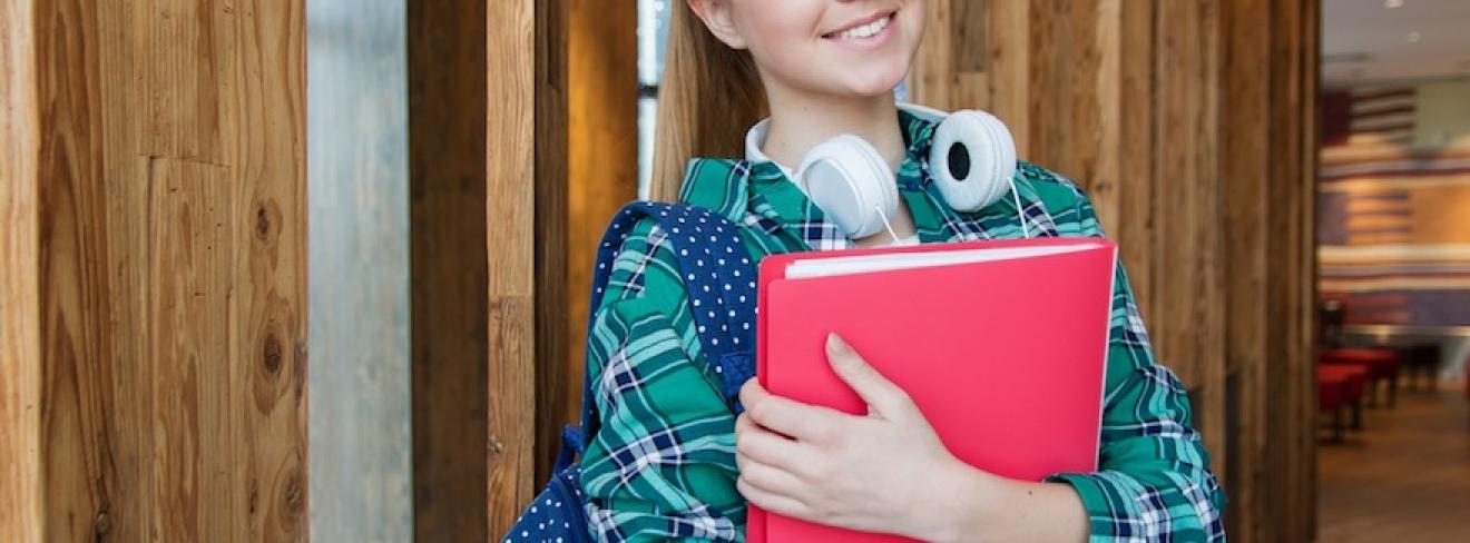 A young woman standing in the hallway, holding school books and smiling at the camera